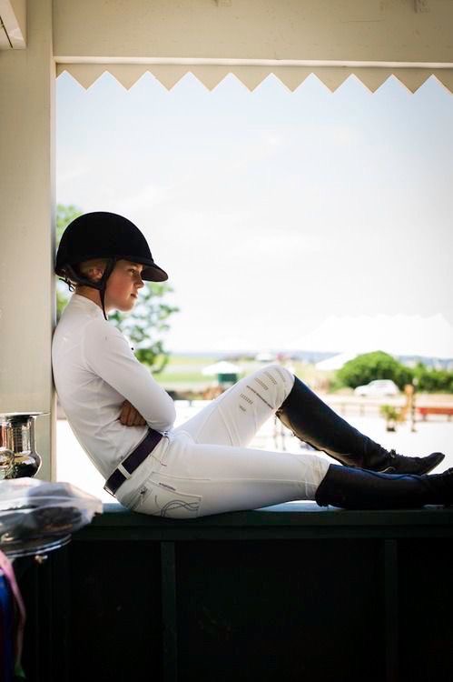 Young rider in a helmet and show whites resting in a doorway between classes